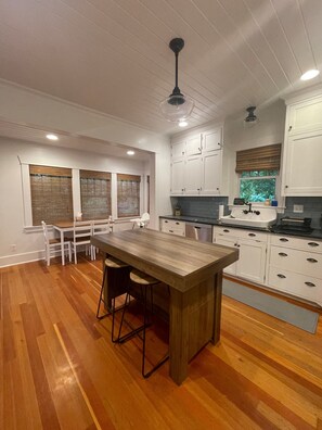 A modern kitchen with white cabinetry, a wooden island, and a dining area with chairs.