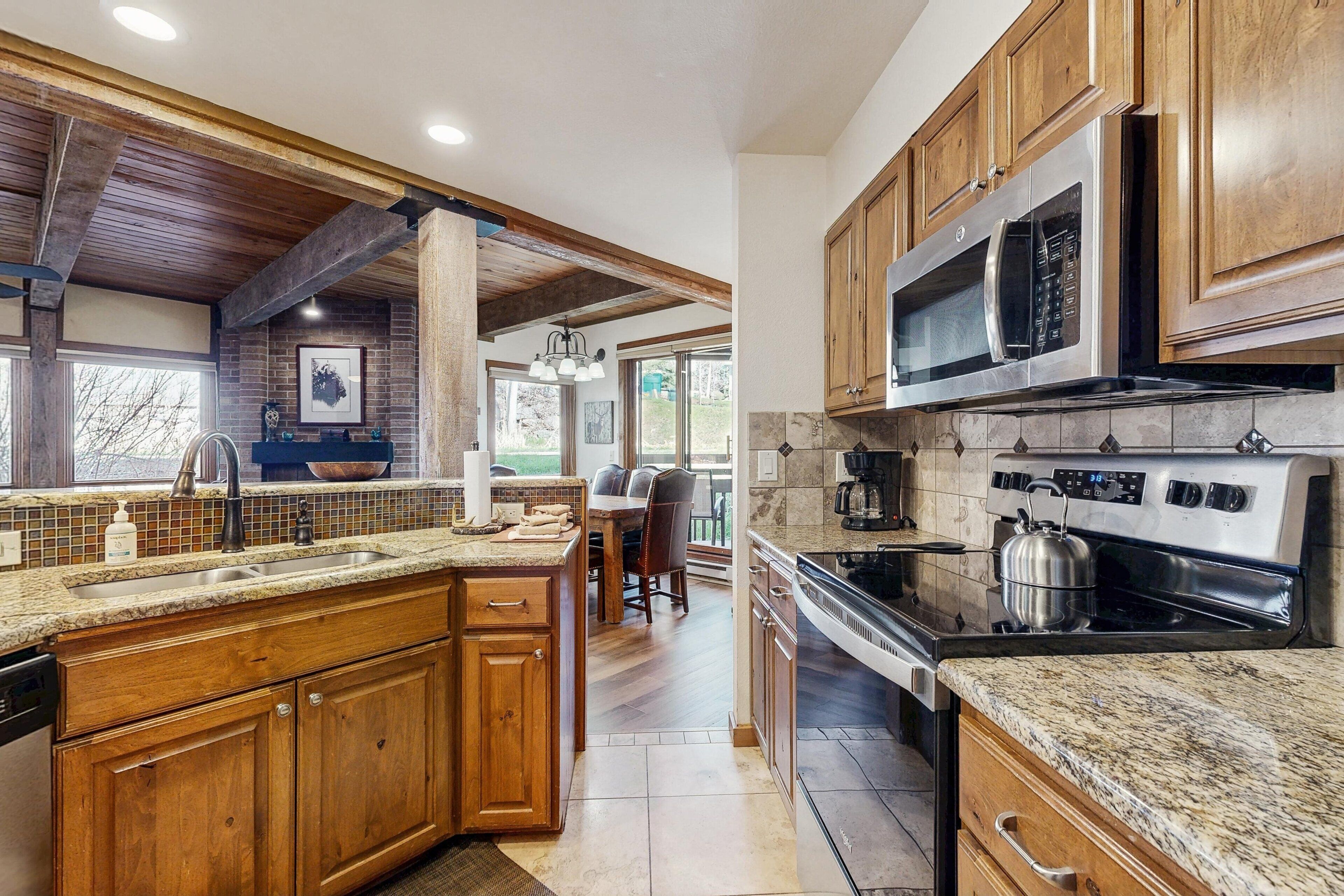 A kitchen with wooden cabinets, granite countertops, a stainless steel oven, and a large window.