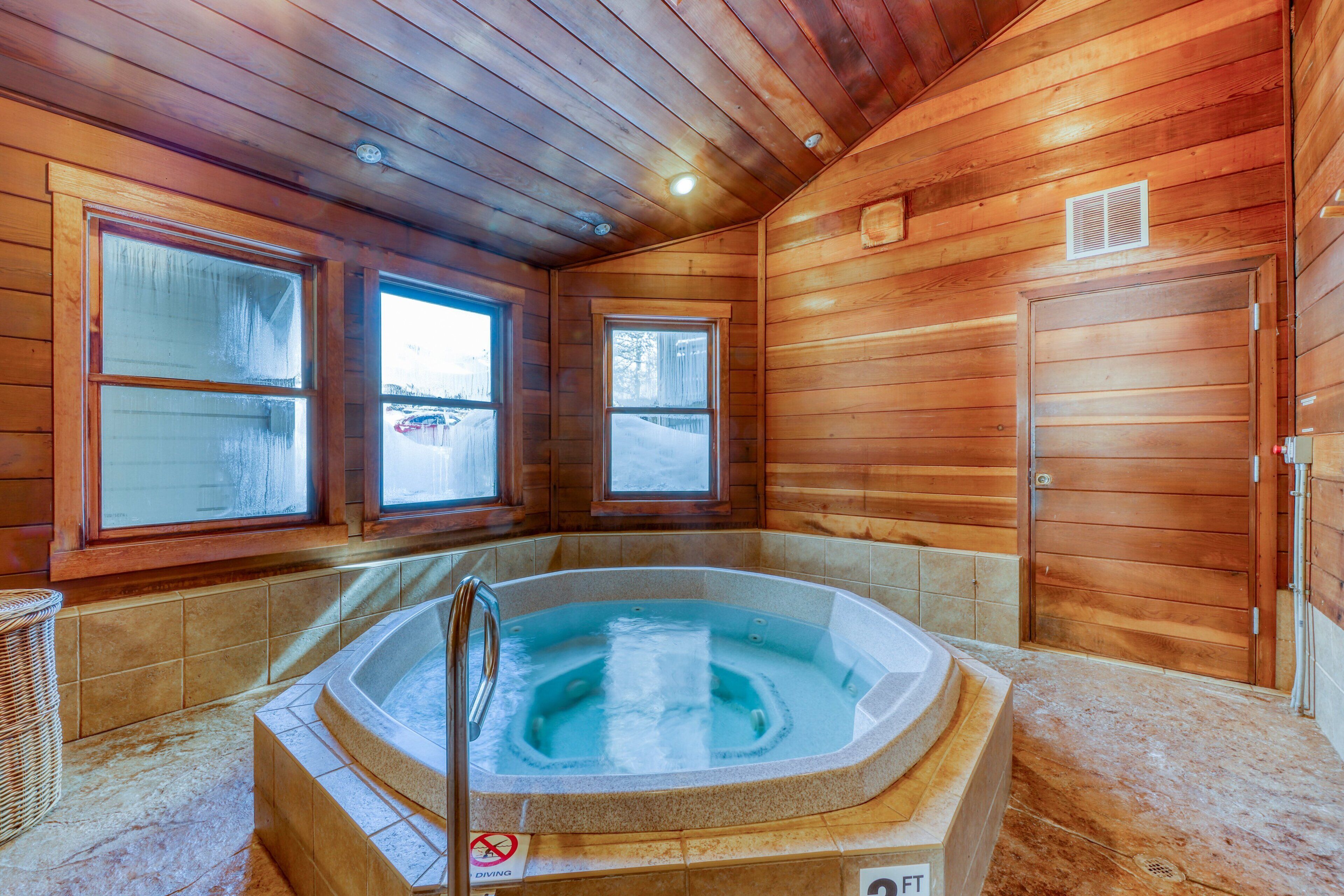 A wooden cabin interior with a hot tub, two windows, and a door.