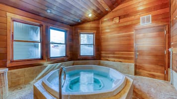 A wooden cabin interior with a hot tub, two windows, and a door.