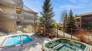 A pool area with two pools, a covered seating area, and a building with balconies.