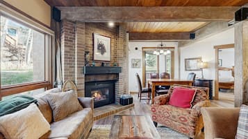 A cozy living room with a fireplace, wooden beams, and a dining area.