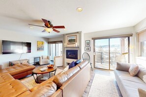 A modern living room with leather sofas, a flat-screen TV, and a balcony with a view. - Large updated condo with full kitchen & private balcony - near resort trails (Steamboat Springs)