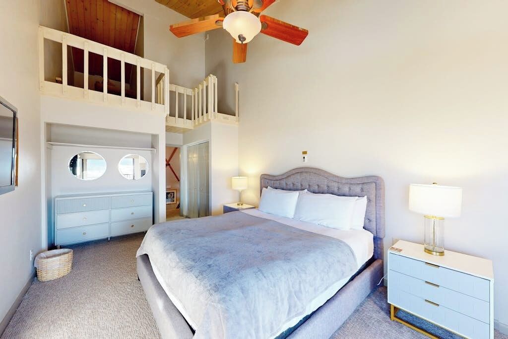 A bedroom with a bed, a nightstand, a dresser, a ceiling fan, and a loft space.