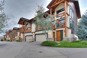 A row of log cabin-style homes with multiple stories, large windows, and a stone foundation. - Large family townhome with pool, hot tubs, tennis court, balcony, & deck (Steamboat Springs)