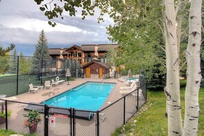 A swimming pool with lounge chairs, a fenced deck area, and a building with a sloped roof in the background. - Cross Timbers #2706 corner townhome with garage and primary suite balcony (Steamboat Springs)