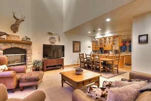 A living room with a fireplace, television, and dining area. - Large family townhome with pool, hot tubs, tennis court, balcony, & deck (Steamboat Springs)