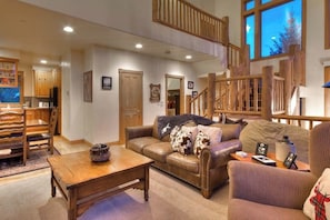A spacious living area with a wooden staircase, a leather sofa, a wooden coffee table, and a dining set. - Large family townhome with pool, hot tubs, tennis court, balcony, & deck (Steamboat Springs)