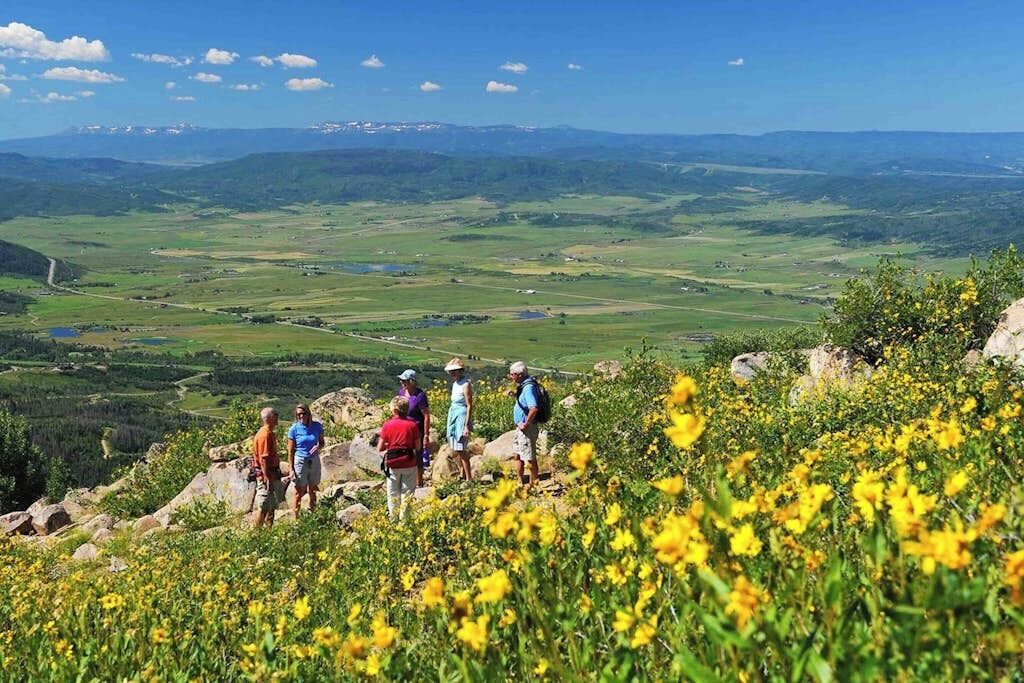 Un groupe de personnes se trouve au sommet d’une colline, d’où elles dominent une vallée parsemée de champs et bordée de montagnes lointaines.