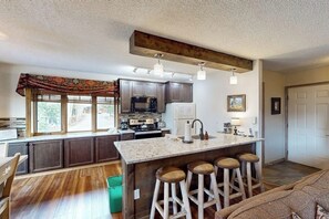 A kitchen with dark cabinets, a central island with stools, a large window, and a ceiling with exposed beams. - Intimate condo with fireplace, washer/dryer, outdoor pool & hot tub (Steamboat Springs)