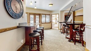 A bar area with stools, a large wall clock, and a staircase. - Intimate condo with fireplace, washer/dryer, outdoor pool & hot tub (Steamboat Springs)