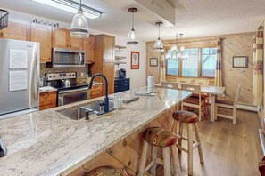 Eine Küche mit Granit Arbeitsplatten, Holzschränken, einem Edelstahl-Kühlschrank, einer Mikrowelle und einem Spülbecken. Es gibt Barhocker und einen Esstisch mit Stühlen.