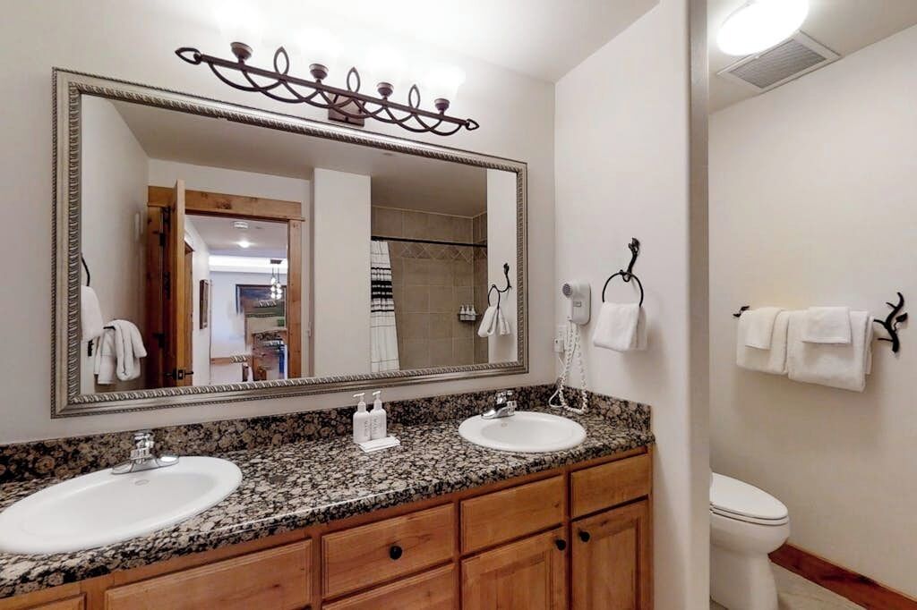 Une salle de bain avec deux lavabos, un grand miroir et des toilettes.