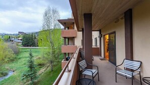 Ein Balkon mit Sitzgelegenheit, Blick auf eine grüne Landschaft und ein mehrstöckiges Gebäude.