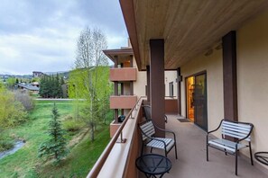 Ein Balkon mit Sitzgelegenheit, Blick auf eine grüne Landschaft und ein mehrstöckiges Gebäude.