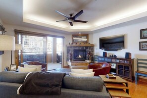 A living room with a sofa, chairs, a fireplace, a TV, and a ceiling fan. - Canyon Creek A204 - Condo w/ creekside views, shared pool, & gym - just 200 yards to the gondola (Steamboat Springs)