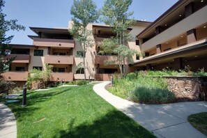 A multi-story building with balconies, a landscaped garden, and a pathway. - Corner condo w/ shared pool & gym - 200 yards from the gondola (Steamboat Springs)