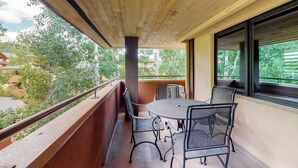 Un balcon avec une table ronde et des chaises, un plafond en bois et une vue sur la verdure et les bâtiments.