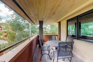 A balcony with a round table and chairs, a wooden ceiling, and a view of greenery and buildings. - Corner condo w/ shared pool & gym - 200 yards from the gondola (Steamboat Springs)