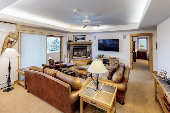A living room with a fireplace, leather sofas, a television, and a ceiling fan. - Corner condo w/ shared pool & gym - 200 yards from the gondola (Steamboat Springs)