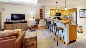 A modern living room with a TV, leather sofa, and a dining area with bar stools. - Canyon Creek A103 - Modern, spacious condo w/ a shared pool, hot tub, & gym - close to the slopes (Steamboat Springs)