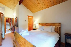 A bedroom with a wooden bed, a nightstand, a lamp, and a door leading to a staircase. - Large split-level condo with valley & mountain views plus hot tubs (Steamboat Springs)