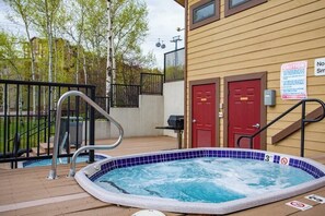 A hot tub with a wooden deck, a metal ladder, and a red door. - Large split-level condo with valley & mountain views plus hot tubs (Steamboat Springs)
