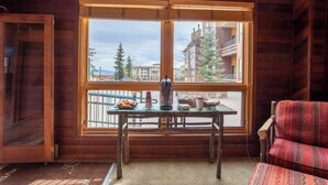 A wooden cabin room with a large window, a table with items, and a patterned sofa. - Kutuk 303 - Spacious, top-floor condo near ski area w/ mountain views plus shared hot tubs (Steamboat Springs)