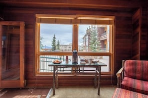 A wooden cabin room with a large window, a table with items, and a patterned sofa. - Spacious, top-floor condo near ski area w/ mountain views plus shared hot tubs (Steamboat Springs)