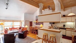 A modern kitchen with a bar area, wooden ceiling beams, and a dining area with a sofa and chairs. - Kutuk 303 - Spacious, top-floor condo near ski area w/ mountain views plus shared hot tubs (Steamboat Springs)