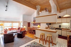 A modern kitchen with a bar area, wooden ceiling beams, and a dining area with a sofa and chairs. - Spacious, top-floor condo near ski area w/ mountain views plus shared hot tubs (Steamboat Springs)