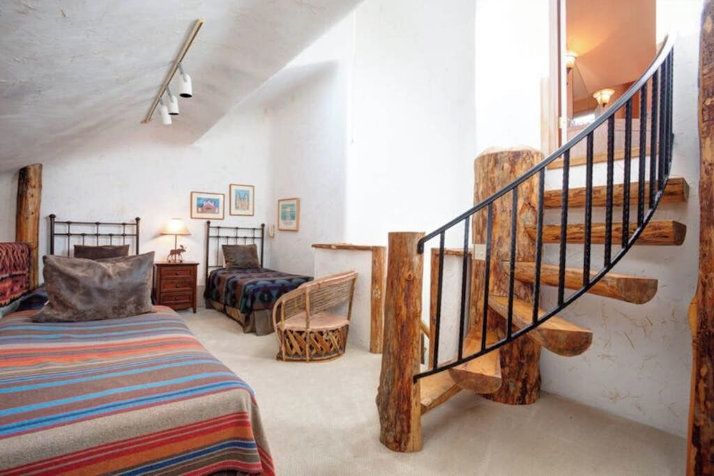 Ein Schlafzimmer mit einem Bett, einem Sessel, einer Holztreppe und einem Nachttisch.