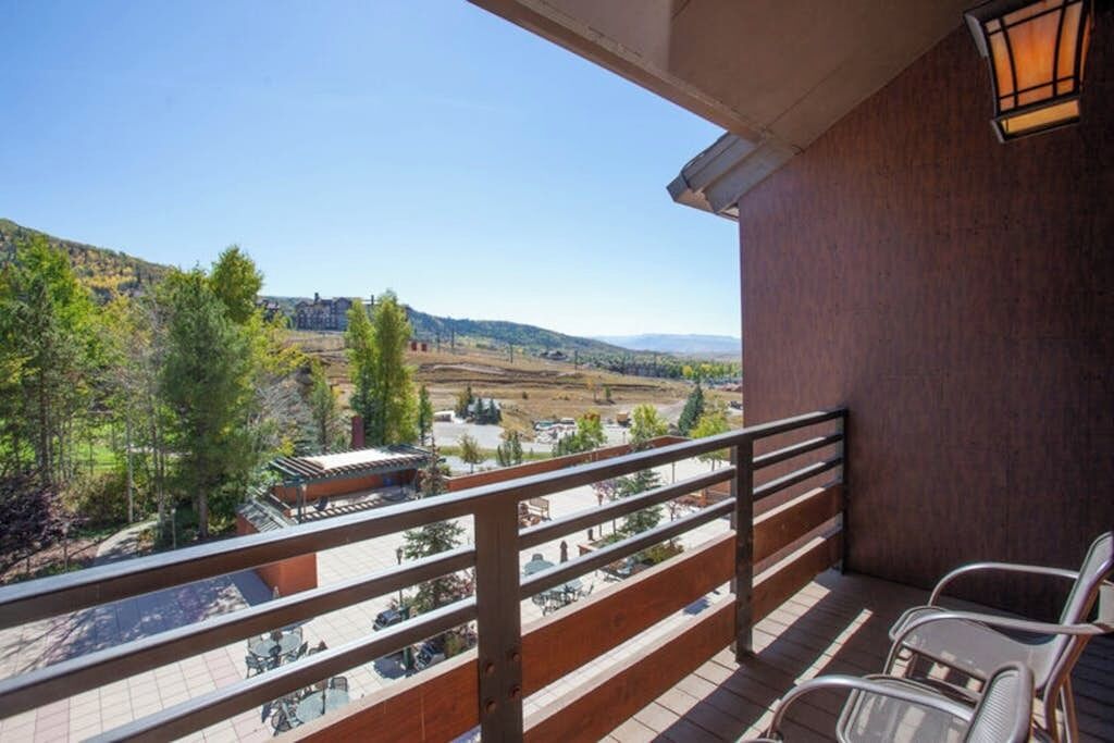 Un balcón con vistas a un valle, baranda de madera y una mesa con sillas.