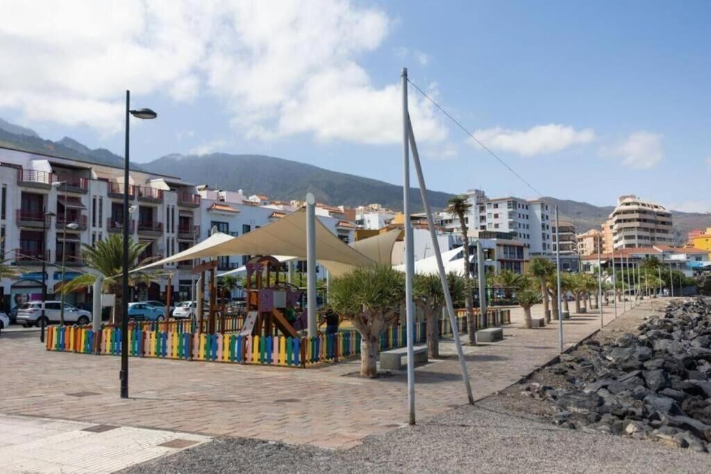 Uma passarela pavimentada com um parquinho, edifícios ao fundo e céu claro.