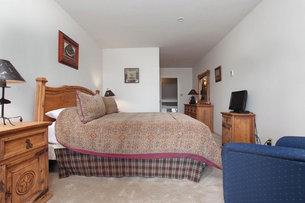 A bedroom with a bed, a wooden dresser, a television, and a blue chair.