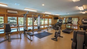Et fitnesscenter med forskellig træningsudstyr, store vinduer og udsigt til grøn natur.