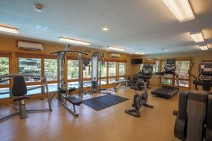 Ein Fitnessstudio mit unterschiedlichen Trainingsgeräten, großen Fenstern und Blick auf Grünflächen.