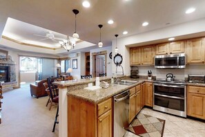 A kitchen with wooden cabinets, a granite countertop, stainless steel appliances, and a dining area with a fireplace. - Top-floor condo w/ great deck & shared pool - short walk to lifts & restaurants (Steamboat Springs)