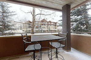 Ein Balkon mit einem Metalltisch und -stühlen, der auf eine verschneite Landschaft mit Gebäuden blickt.