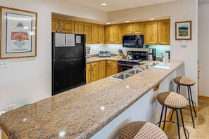 A kitchen with wooden cabinets, a black refrigerator, a microwave, a stove, and a granite countertop. - Second floor condo with gas fireplace, WiFi, pool, and hot tub - walk to gondola (Steamboat Springs)
