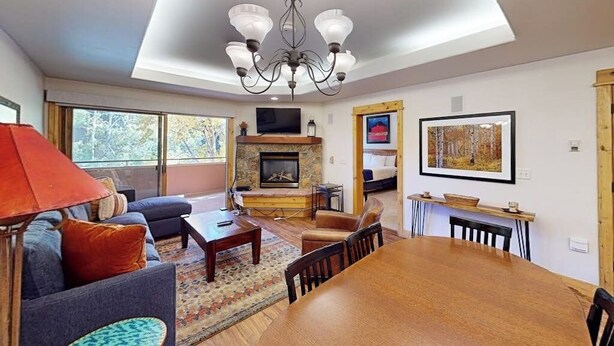A spacious living room with a fireplace, a chandelier, and a dining area. - Canyon Creek B207 - Modern family getaway w/ a pool, pool spa, garage parking - walk to the gondola (Steamboat Springs)