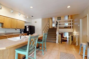 A kitchen with wooden cabinets, a central island with chairs, a staircase, and a dining area. - Cozy, mountain condo with full kitchen & living area plus hot tubs (Steamboat Springs)