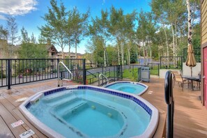 A deck with two hot tubs, a pool, and a fenced area with trees. - Cozy, mountain condo with full kitchen & living area plus hot tubs (Steamboat Springs)