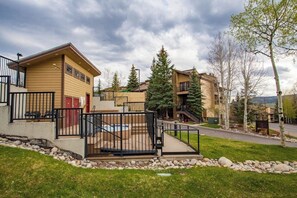 A residential building with a swimming pool, a fenced patio, and a staircase leading to the entrance. - Cozy, mountain condo with full kitchen & living area plus hot tubs (Steamboat Springs)