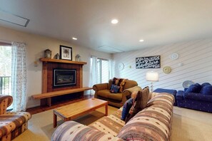A living room with a fireplace, a sofa set, a coffee table, and a wall-mounted TV. - Cozy, mountain condo with full kitchen & living area plus hot tubs (Steamboat Springs)