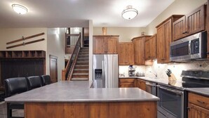 A kitchen with wooden cabinets, a stainless steel refrigerator, a microwave, a stove, and a bar area with stools. - Kutuk 212 - Recently remodeled condo close to the base area w/ shared hot tubs & firepit (Steamboat Springs)