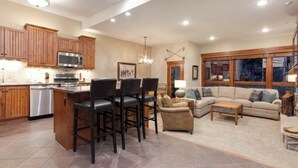 A spacious living area with a kitchen, dining area, and a large window with a view. - Kutuk 212 - Recently remodeled condo close to the base area w/ shared hot tubs & firepit (Steamboat Springs)