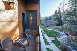 Ein Holzhaus mit Veranda, zwei Stühlen und Blick auf Bach und Wald.