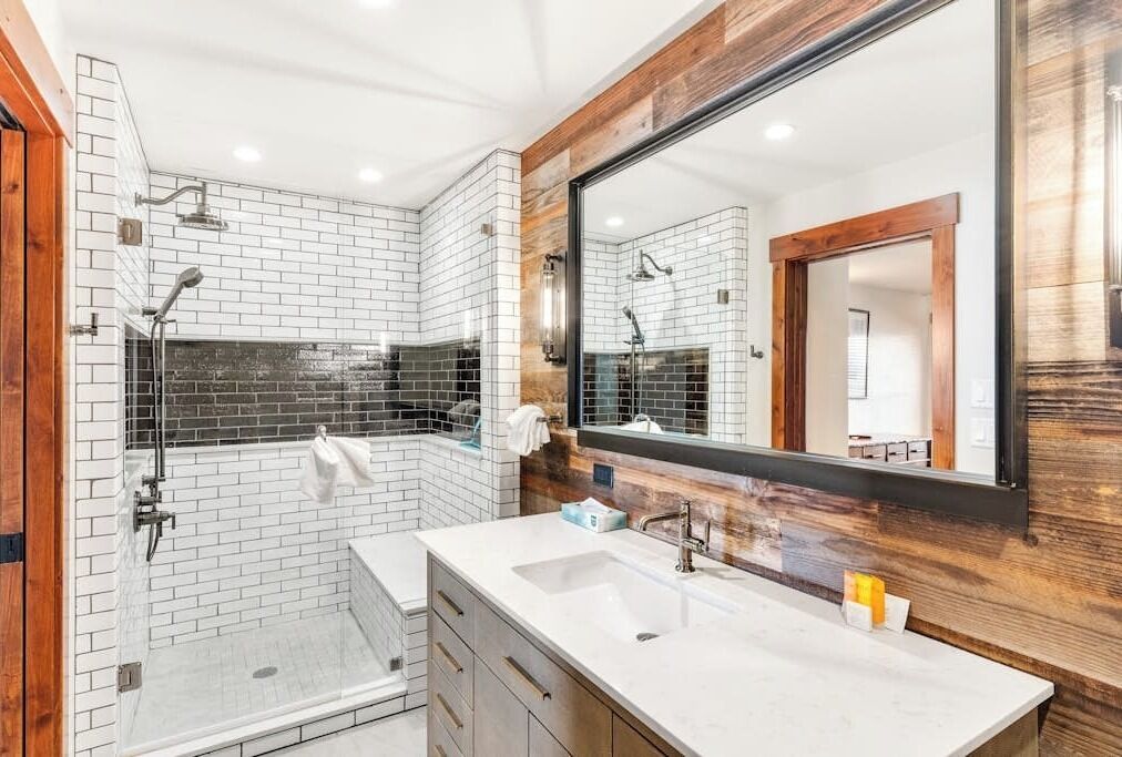 Een moderne badkamer met een douchecabine van glas, een grote spiegel en een wit wastafelmeubel.