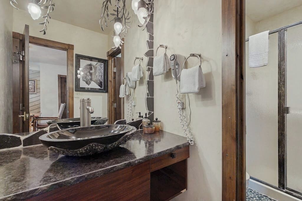 Un baño con lavamanos de granito negro, un espejo y cabina de ducha.
